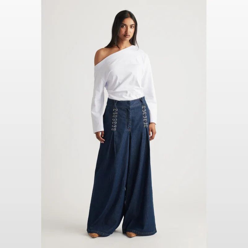 Woman wearing Decjuba Devina High Rise Wide Leg Jeans in dark wash denim, featuring a high waist, wide leg silhouette, and decorative lace-up detail on the front pockets.