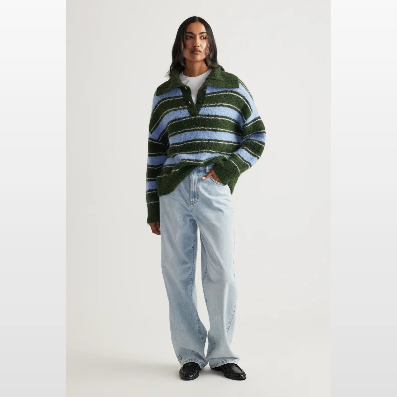 Woman wearing a green and blue striped knit polo jumper with a collared neckline and button front, paired with light wash wide-leg jeans.