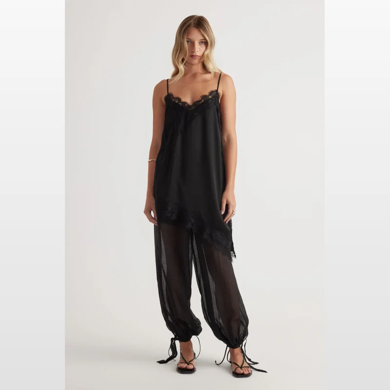 Woman wearing Decjuba black lace-trimmed slip camisole and sheer black balloon pants with adjustable ties at the cuffs.