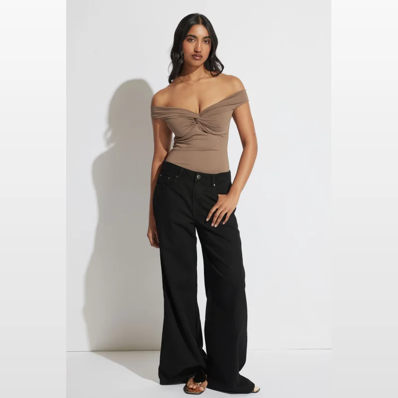 Model wearing a brown off-the-shoulder twist front top by Decjuba, paired with black wide-leg jeans.