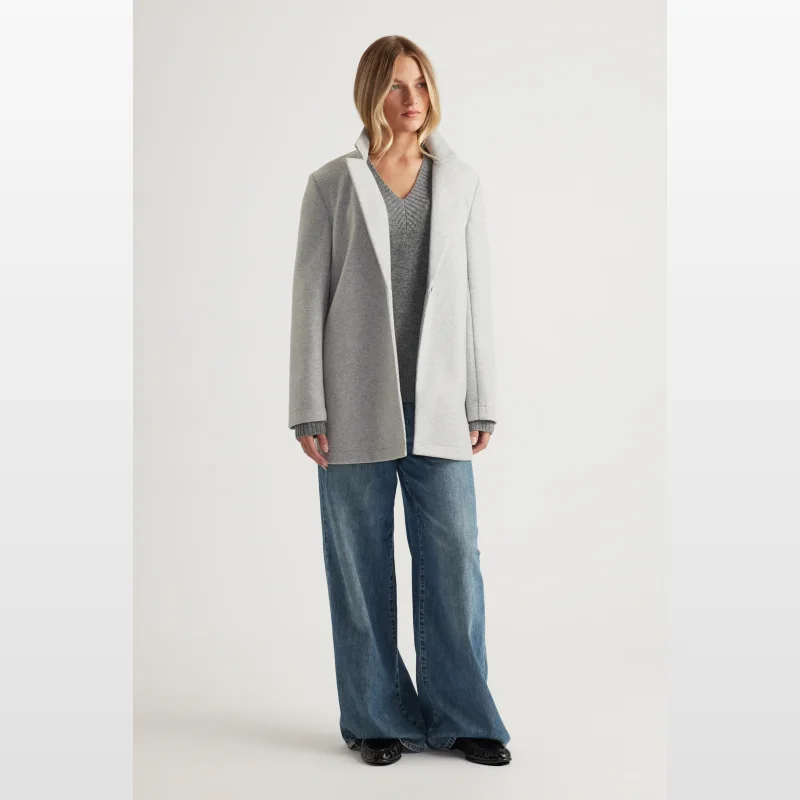Woman wearing a mid-length grey felt coat with a collared neckline, over a grey v-neck jumper and wide-leg blue jeans.