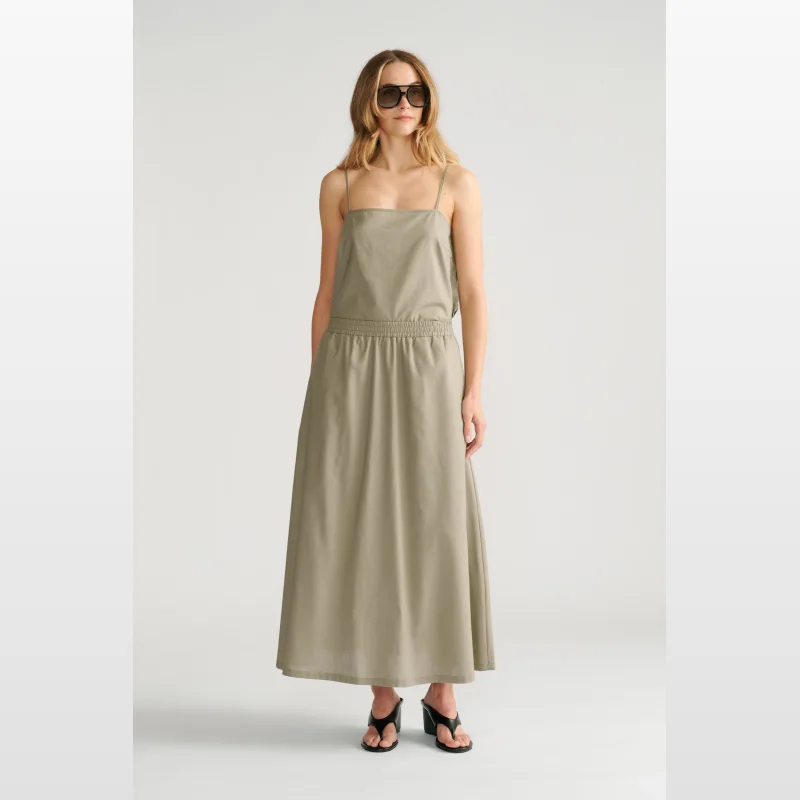 Woman wearing a light olive green midi skirt with an elasticated waist and spaghetti straps, paired with black wedge sandals and sunglasses.