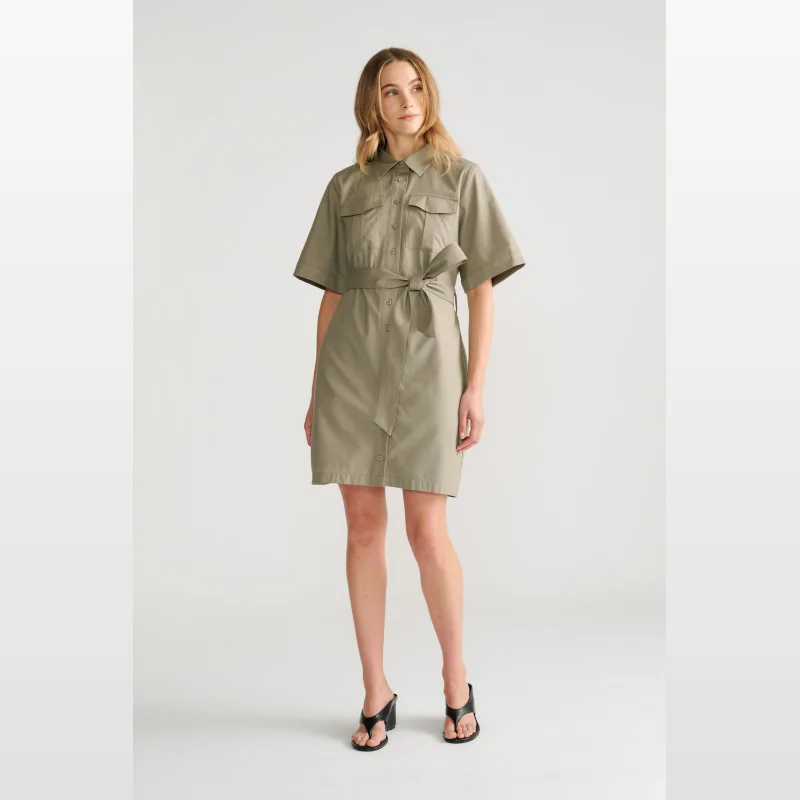 Woman wearing a short-sleeved, collared, olive green mini dress with a tie waist and two chest pockets.