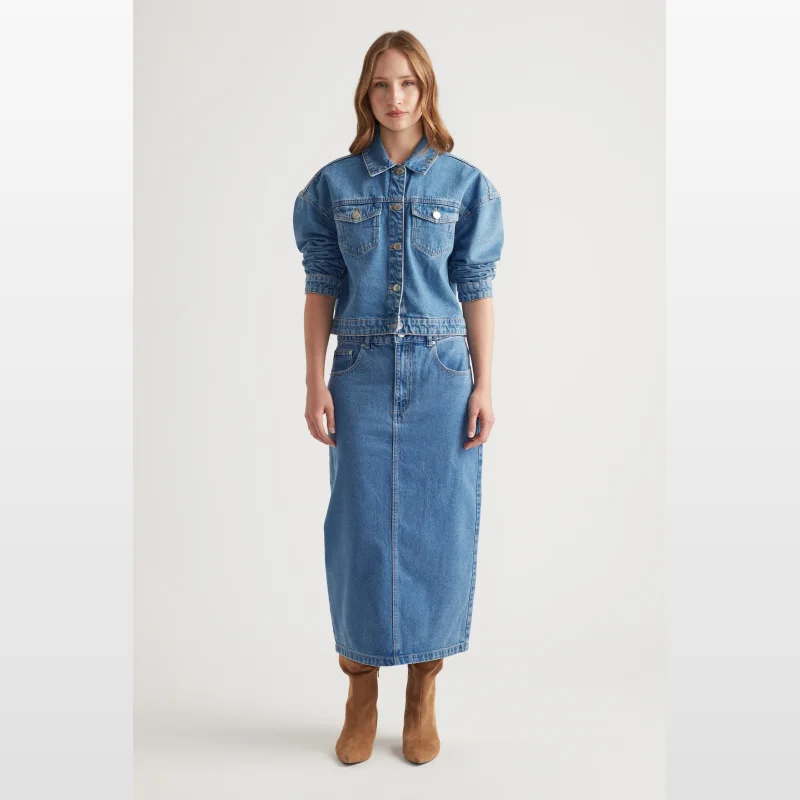 Woman wearing a blue denim midi skirt and matching denim jacket, standing against a white background.