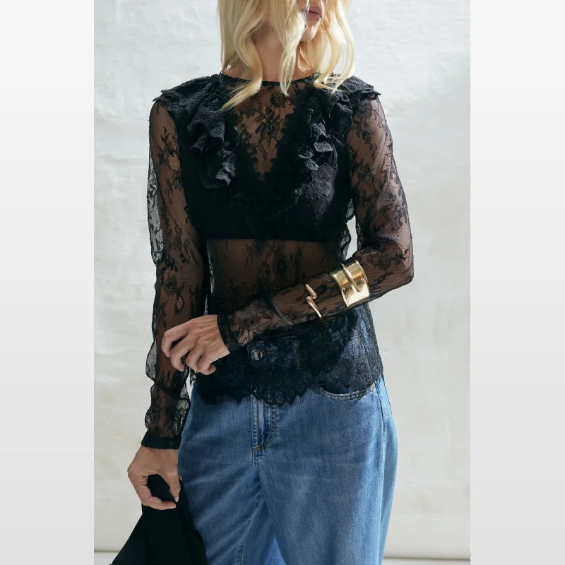 Woman wearing a black long-sleeved lace top with ruffle details and a crew neckline, paired with blue denim jeans.
