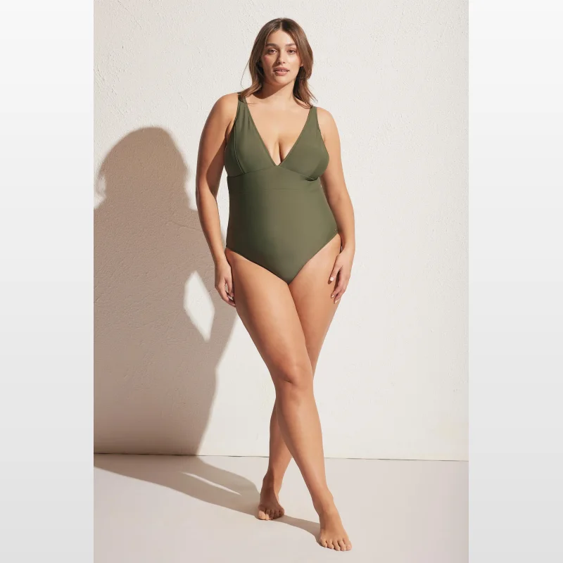 Woman wearing a matte olive green V-neck one-piece swimsuit with adjustable straps and medium brief coverage.