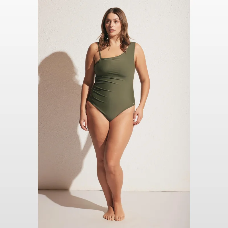 Woman wearing a khaki green one-shoulder one-piece swimsuit with ruching detail and gold hardware.