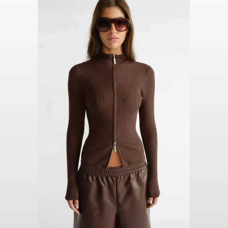 Woman wearing a fitted brown ribbed knit long sleeve top with a high neckline and a silver double-ended zipper closure.