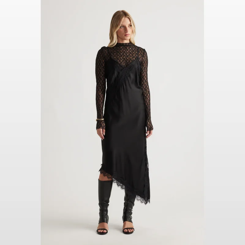 Woman wearing a black lace trim midi slip dress with adjustable straps and an asymmetric hem, paired with black knee-high heeled sandals.