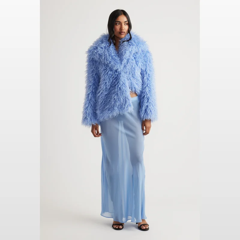 Woman wearing a light blue sheer maxi skirt with an elasticated waistband, paired with a fluffy blue jacket.