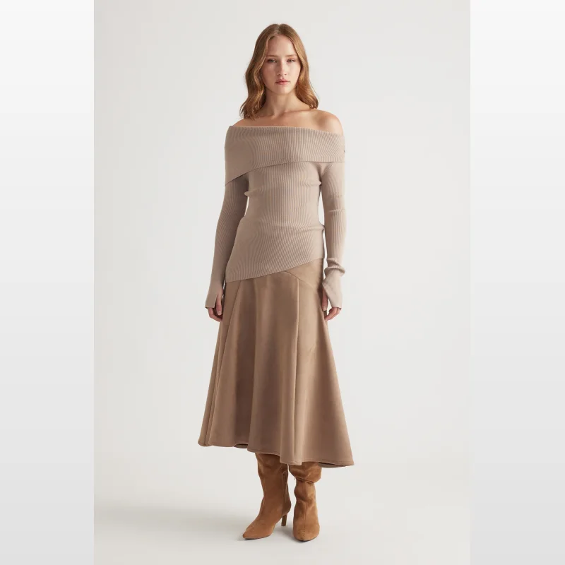 Woman wearing a taupe off-shoulder ribbed knit top with long sleeves and an asymmetrical hem, paired with a tan midi skirt and brown boots.
