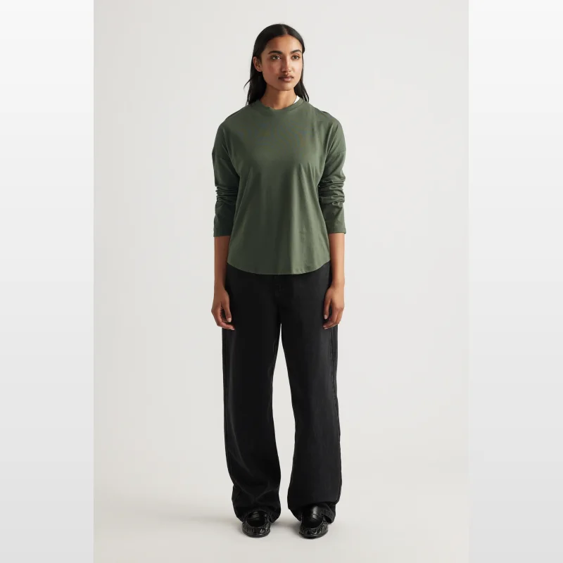 Woman wearing a green long sleeve crew neck top with drop shoulders and a scooped hem, paired with black wide-leg jeans.