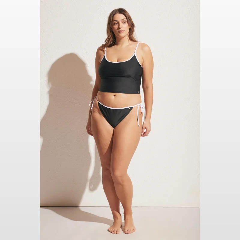 Woman wearing a black Decjuba contrast tie bikini bottom with white piping and adjustable side ties.