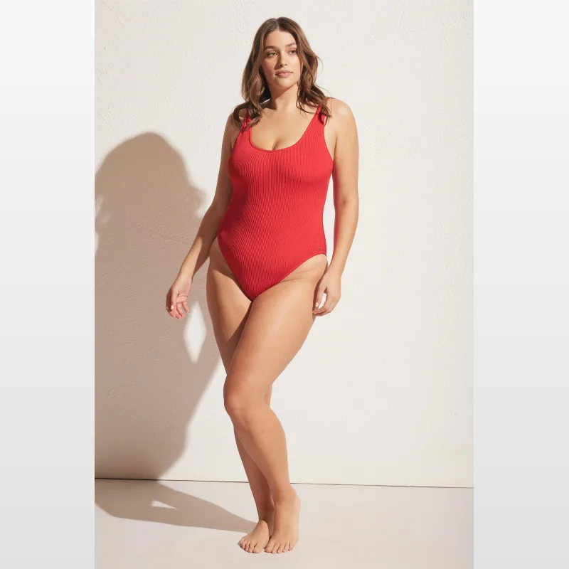 Woman wearing a red crinkle fabric scoop neck one-piece swimsuit with a low scoop back.