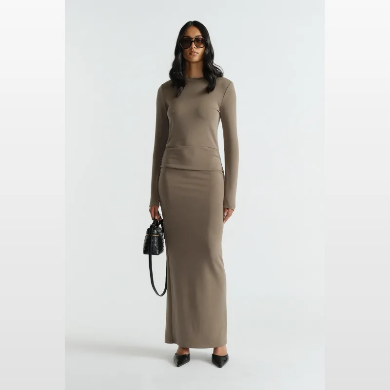 Woman wearing a long-sleeved, taupe midi dress with side ruching and a back hem split, paired with black heels and sunglasses.