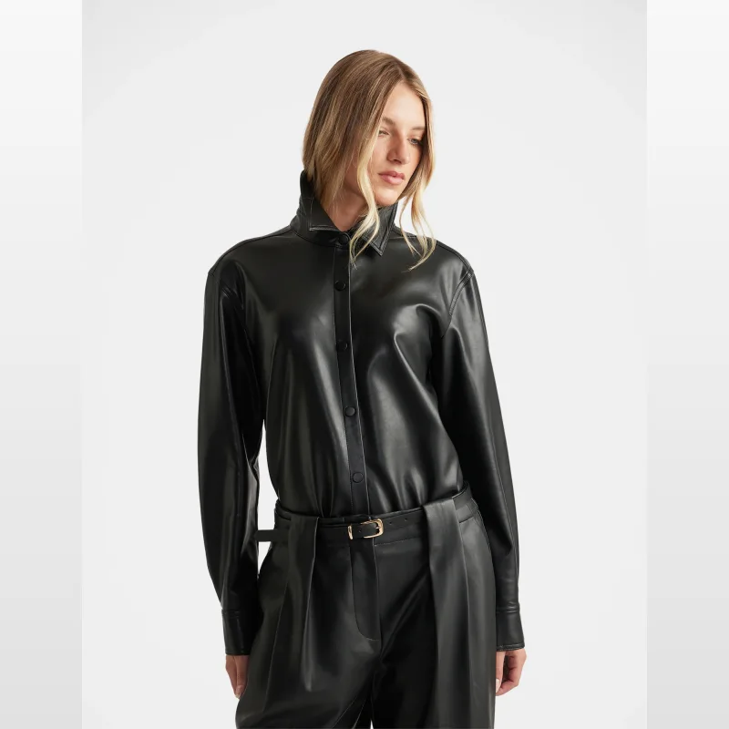 Woman wearing a black faux leather collared shirt with full-length sleeves and button-through front.