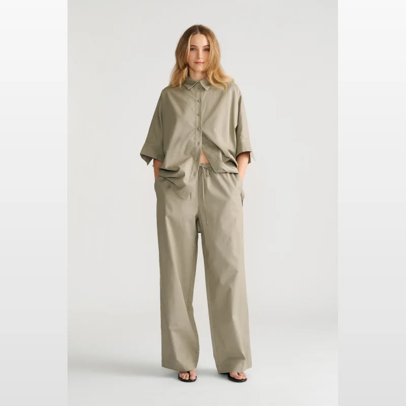 Woman wearing Decjuba Abbey Pull On Pant in a light olive green colour. The pants are high-waisted with an elasticated drawcord waist and a wide leg silhouette.