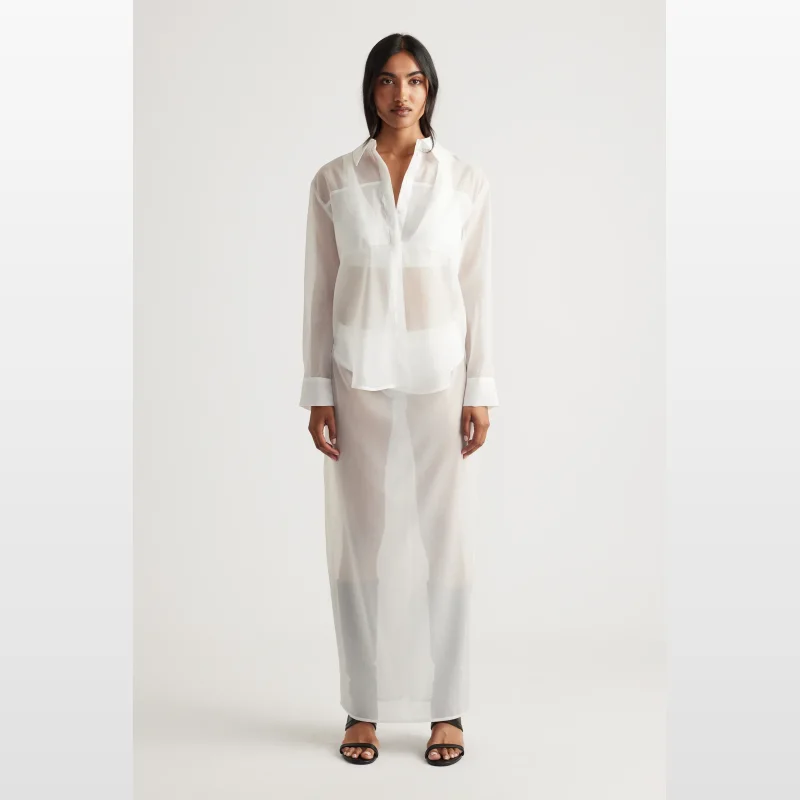 Woman wearing a white sheer organza long-sleeved button-up shirt over white lingerie, with a matching sheer skirt.