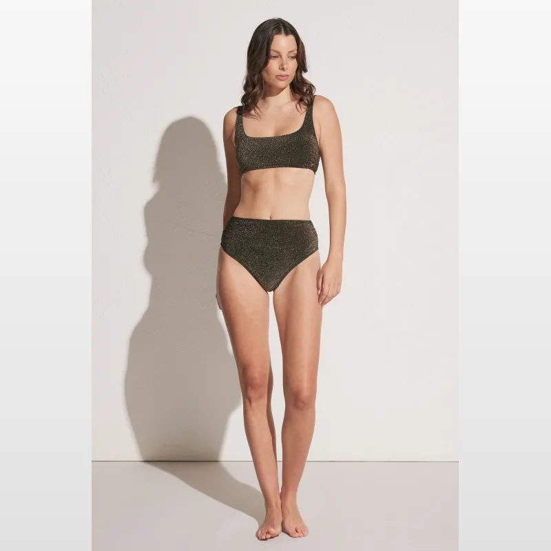 Woman wearing a shimmering gold high-rise bikini bottom with gathered detailing.