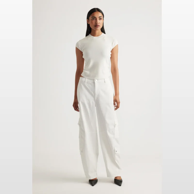 Woman wearing a white Decjuba Lily Pleat Detail Knit Tee with cap sleeves and a round neckline, paired with white cargo pants.
