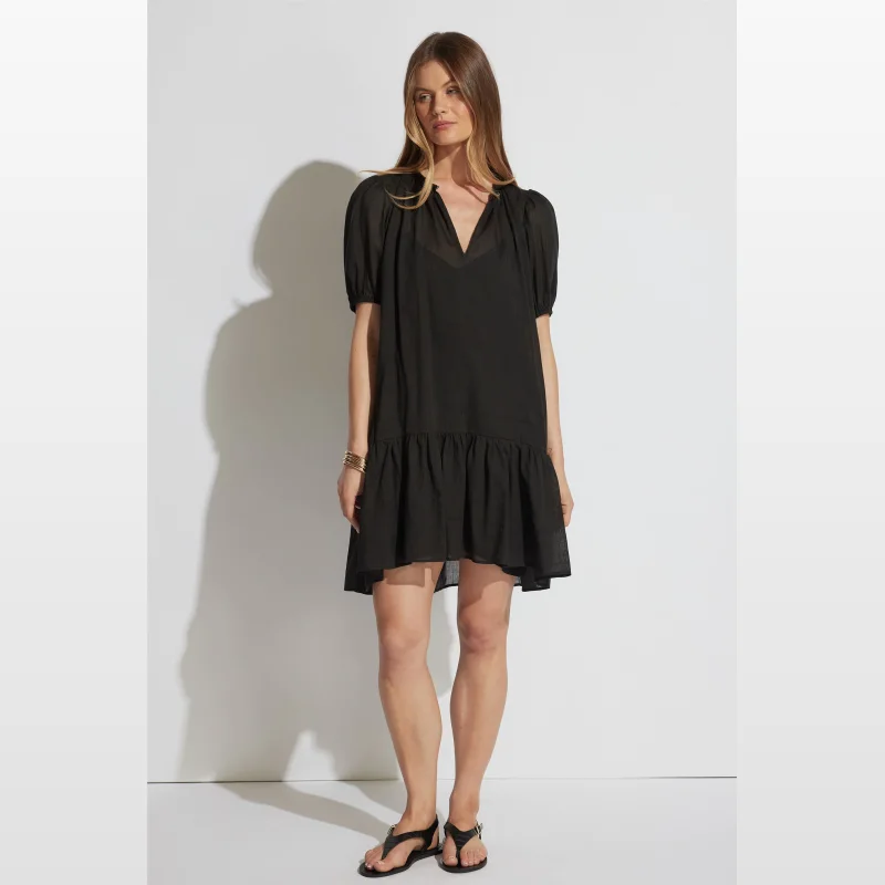 Woman wearing a black Decjuba Dalia Mini Dress with puff sleeves and a tiered hem.