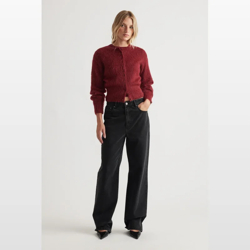 Woman wearing a fitted, burgundy, textured knit, crew neck, long sleeve cardigan with button through front, paired with black wide-leg jeans.
