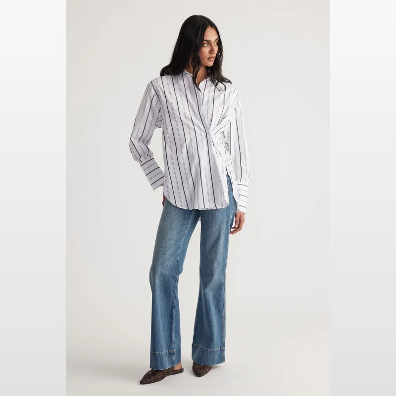 Woman wearing a white and black striped long-sleeve button-up shirt with a collared neckline and a relaxed fit, paired with blue denim jeans.