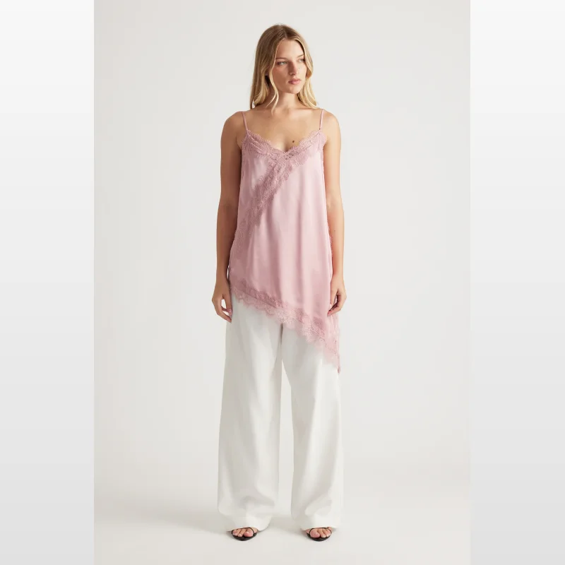 Woman wearing a pink lace trim tunic with thin adjustable straps and an asymmetric hem, paired with white wide-leg pants.