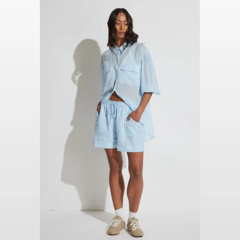 Woman wearing light blue and white striped ramie shorts with an elasticated drawstring waist and side pockets.