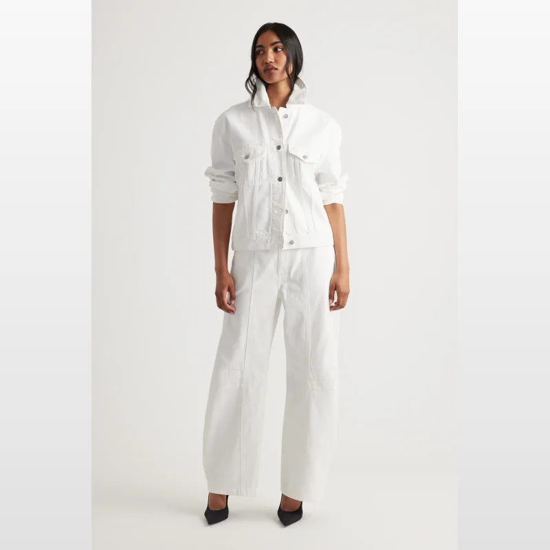 Woman wearing a white Decjuba Nakita denim jacket with a collared neckline, button-through front, and chest pockets. The jacket has an oversized, boxy fit and adjustable waist tabs.