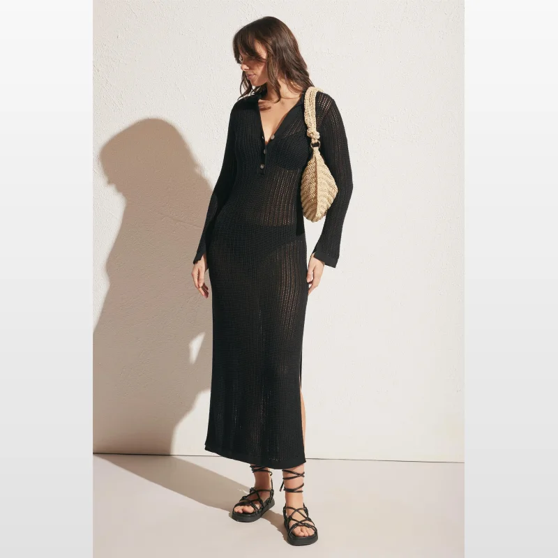 Woman wearing a black long-sleeved crochet midi dress with a collared neckline and side splits, paired with black lace-up sandals and a straw handbag.