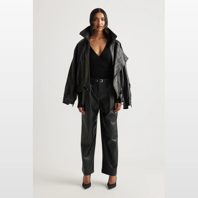 Model wearing Decjuba Tabitha Faux Leather Pants in black, featuring a high waist, pleat detail, and wide leg.