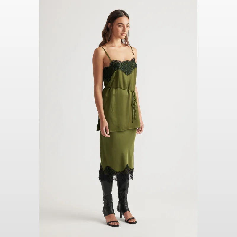 Woman wearing a green satin camisole top with black lace trim and adjustable straps, tied at the waist.