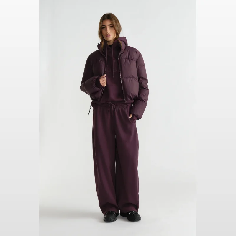 Woman wearing Decjuba D-Luxe Barrel Trackpants in a plum colour, paired with a matching hoodie and puffer jacket.