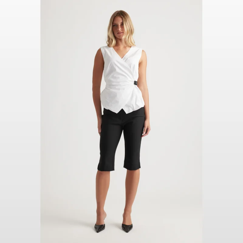 Woman wearing a white sleeveless V-neck wrap top with a belted waist and black capri pants.