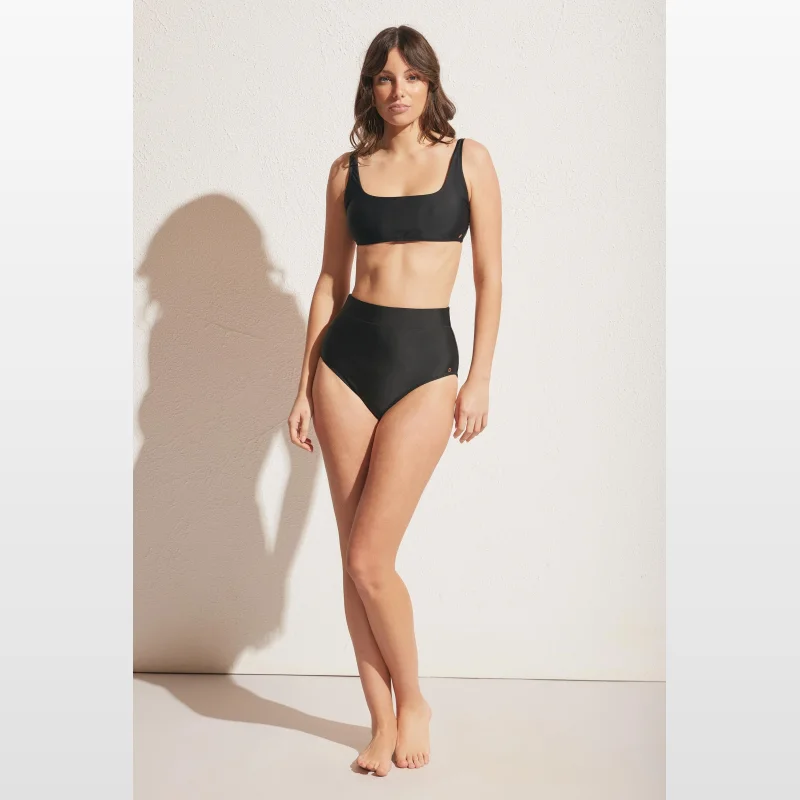 Woman wearing a black Decjuba ultra high waist bikini bottom with full brief coverage.