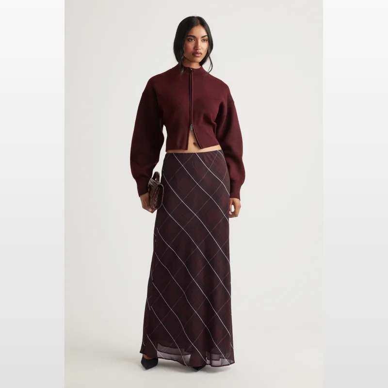 Woman wearing a maroon cropped knit jumper with a high neck and zip-through front, paired with a long plaid skirt.