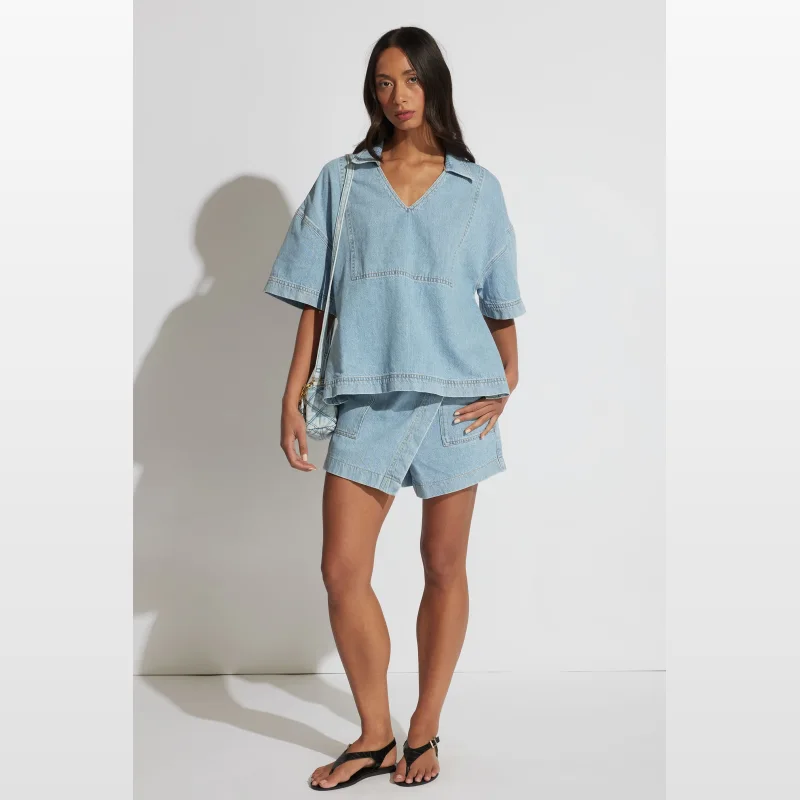 Woman wearing a light blue oversized short-sleeved denim shirt with a V-neckline and collar, paired with matching denim shorts.