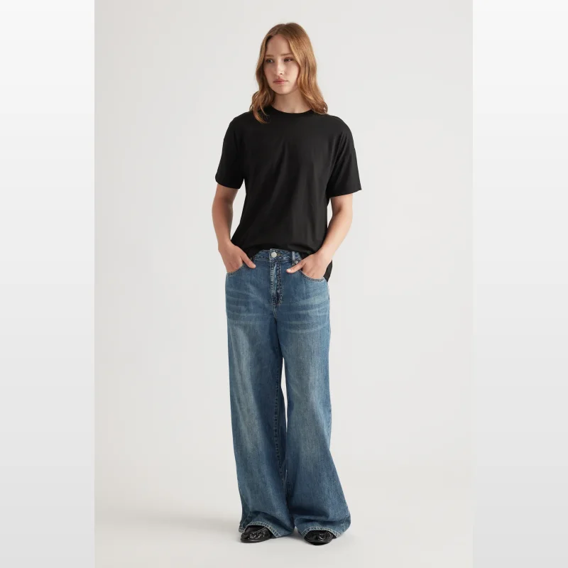 Woman wearing a black short-sleeve crew neck t-shirt with drop shoulders and a relaxed fit, paired with wide-leg blue jeans.