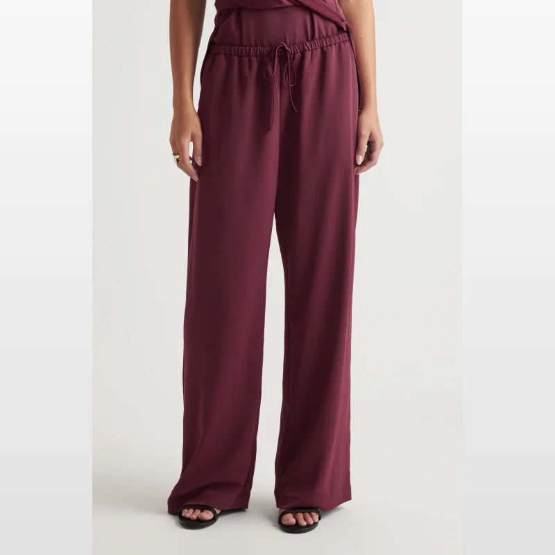 Close-up of a woman wearing burgundy Decjuba Sophie Relaxed Pants, showing the elasticated waistband with a tie and the straight leg silhouette.