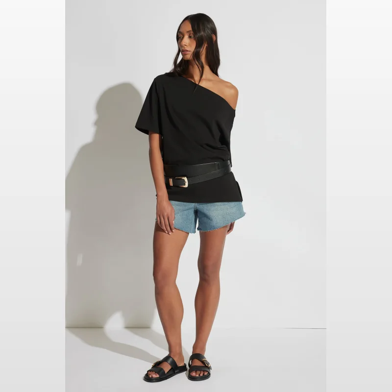Model wearing Decjuba Kylie light wash denim shorts with a raw hem, high rise fit, and a black off-the-shoulder top.