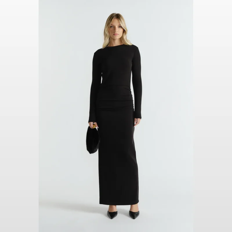 Woman wearing a black long sleeve midi dress with side ruching and a back hem split, holding a black furry clutch bag.