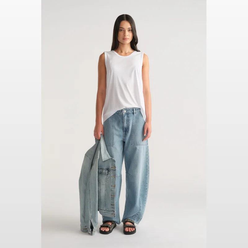 Woman wearing a white D-Luxe Boyfriend Tank by Decjuba with light wash wide-leg jeans and black sandals, holding a denim jacket.