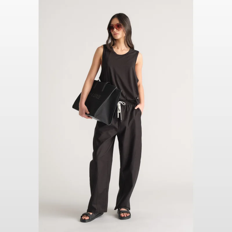 Woman wearing a black D-Luxe Boyfriend Tank with low armholes and a round neckline, holding a black tote bag.