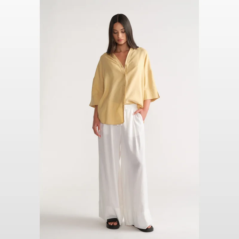 Woman wearing a yellow D-Luxe Linen Blend 3/4 Shirt with a collared neckline and 3/4 sleeves, paired with white wide-leg pants.