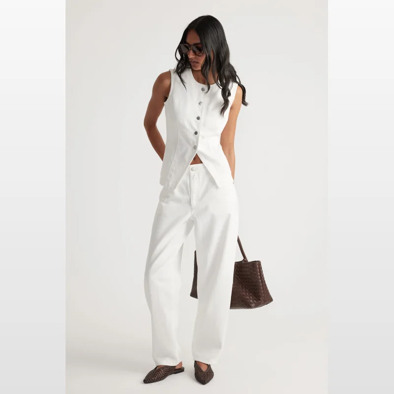 Model wearing a white Chloe denim vest by Decjuba, paired with white jeans and brown woven accessories.