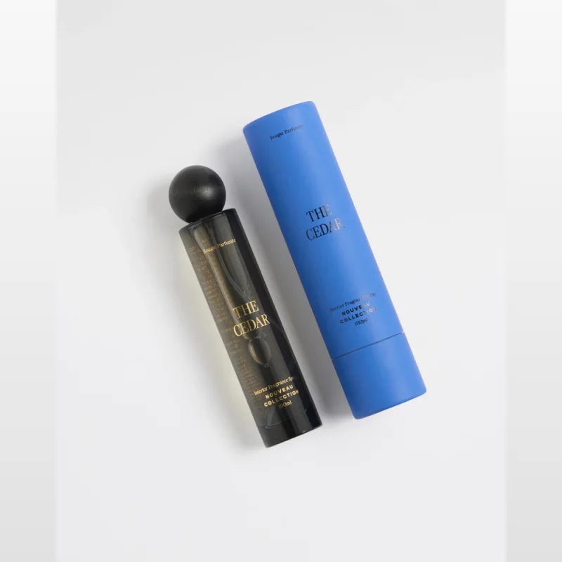 The Cedar 100ml Interior Fragrance by Dusk, presented in a black spray bottle with a black cap, next to its blue cylindrical packaging.
