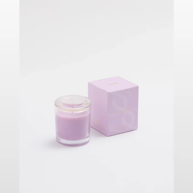 A small, purple scented candle in a clear glass jar with a lid, next to its light purple box, both featuring the Dusk brand and 'Calm' collection details.