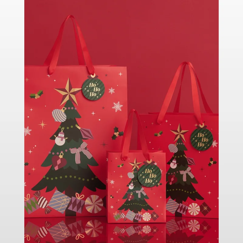 Three red Christmas gift bags of varying sizes, decorated with festive Christmas tree designs, presents, snowflakes, and 'Ho Ho Ho' tags.