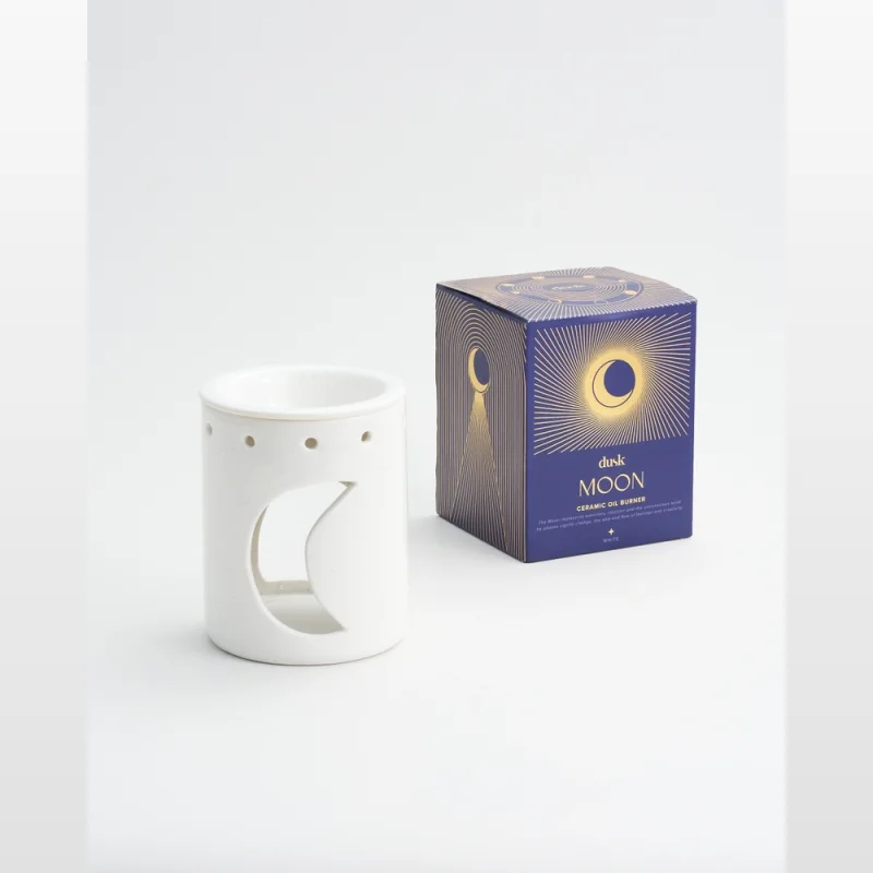 A white ceramic oil burner with a crescent moon cut-out, placed next to its blue and gold 'Moon Ceramic Oil Burner' packaging.